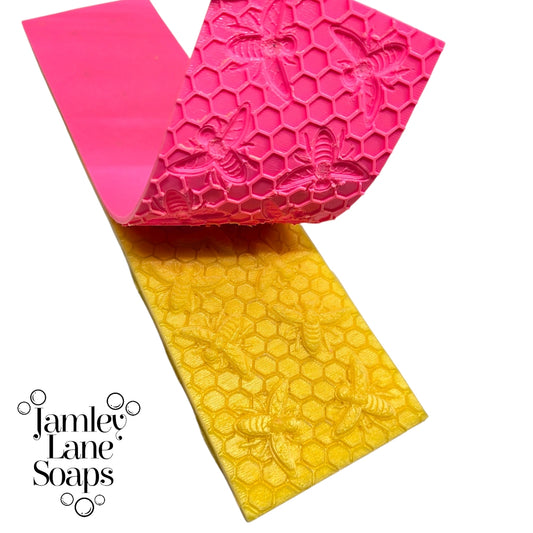 an impression mat peeled back revealing a yellow soap with honeybees on top of a honeycomb pattern