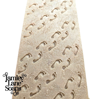 loaf of soap close up featuring the sandy footprints pattern created as a result of the impression mat in the listing and featuring 'Jamley Lane Soaps' branding