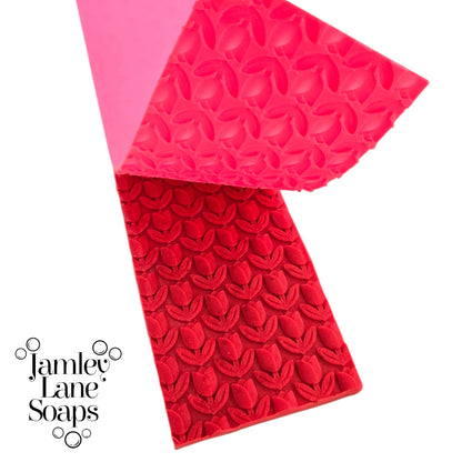 repeating tulip artisan polymer impression mat being peeled back from a red melt and  pour soap top on a white background, branded with 'Jamley Lane Soaps'.